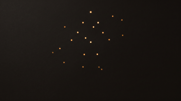 Scattered warm golden light points glowing against a deep black background, resembling stars or fiber-optic lights in a minimalist dark composition